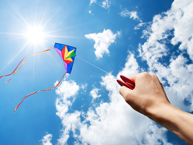 A colorful kite being flown in a blue sky with white clouds.