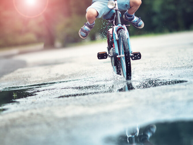 A child rides its bike through a rain puddle.
